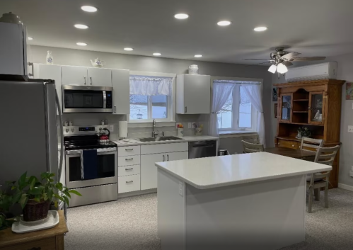 Modern kitchen with white cabinets, stainless steel appliances, an island, and a dining area with a wooden hutch.