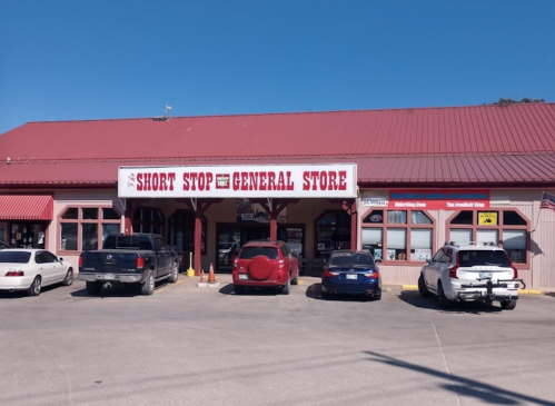 A general store with a red roof and sign, featuring parked cars in front on a sunny day.