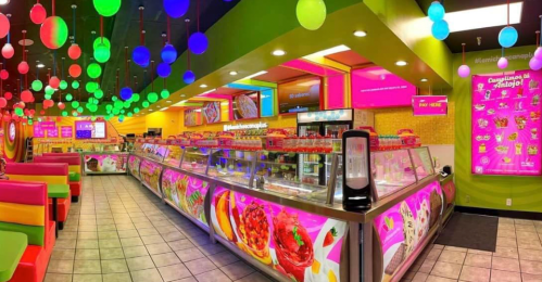 Brightly colored ice cream shop interior with vibrant decor, neon lights, and a display of various ice cream flavors.