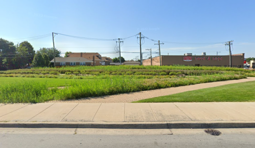 A grassy area with a sidewalk, power lines, and a building in the background, likely a store or restaurant.