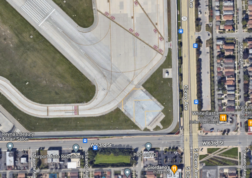 Aerial view of an airport runway with nearby streets and businesses, including a pizza place and auto repair shops.