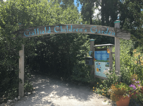 Sign for "Callfield Children's Garden" at the entrance, surrounded by greenery and colorful flowers.