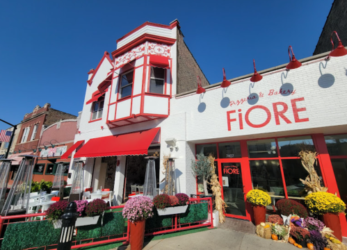 Exterior of Fiore Pizzeria & Bakery, featuring red accents, outdoor seating, and colorful flower arrangements.