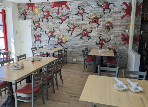 A vibrant restaurant interior featuring playful wall art of cartoonish characters and wooden tables with chairs.