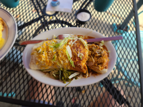 A plate of enchiladas topped with cheese, lettuce, and sauce, served on a black metal table.