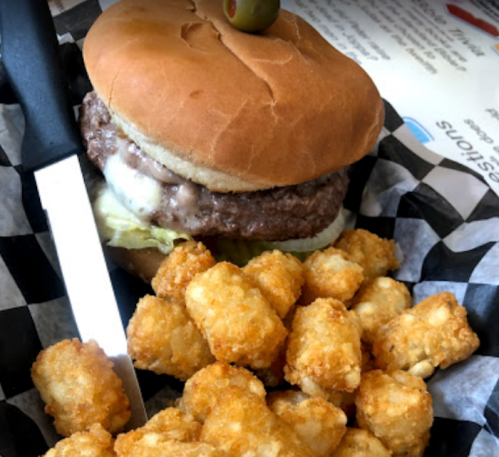 A juicy hamburger with lettuce and cheese, served with a side of crispy tater tots on a checkered paper.