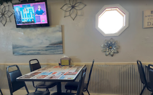 A cozy restaurant interior with a table, chairs, a TV showing a game show, and a decorative window.