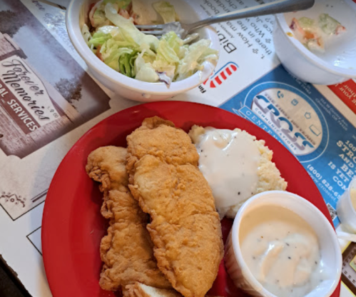 A red plate with three pieces of fried fish, mashed potatoes with gravy, and a side salad in a bowl.
