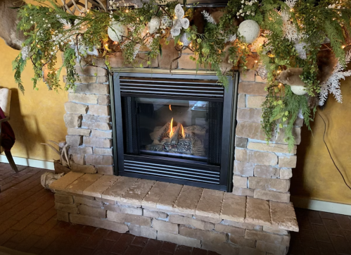 A cozy stone fireplace with a lit fire, decorated with greenery and festive ornaments.