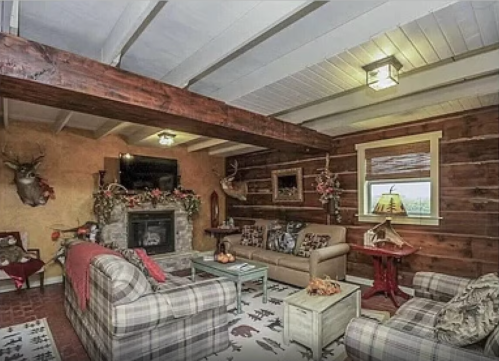 Cozy living room with wooden beams, rustic decor, a fireplace, and comfortable seating.