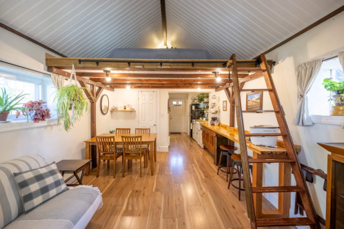 Cozy interior of a small home featuring a loft, dining area, and kitchen with wooden accents and natural light.