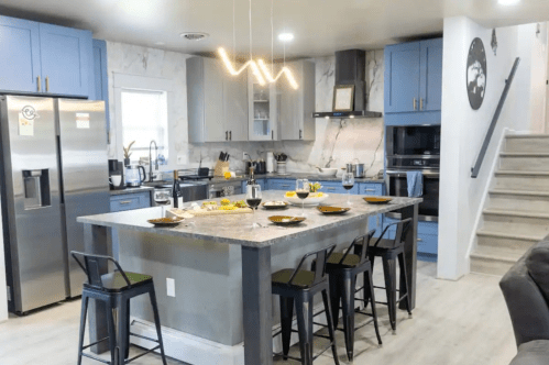 Modern kitchen with blue cabinets, marble countertops, and a large island with seating, featuring a stylish light fixture above.