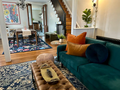 Cozy living room with a green sofa, colorful rug, and dining area visible in the background. Warm, inviting decor.