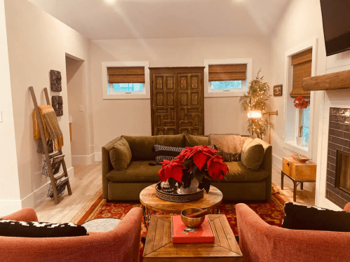 Cozy living room with a green sofa, red chairs, a wooden coffee table, and decorative plants. Warm, inviting atmosphere.