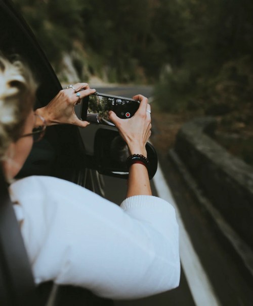 A person taking a photo with a smartphone from a moving car, capturing a scenic view outside.