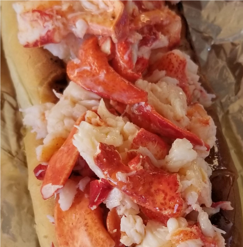 A close-up of a lobster roll filled with chunks of lobster meat on a toasted bun, wrapped in foil.