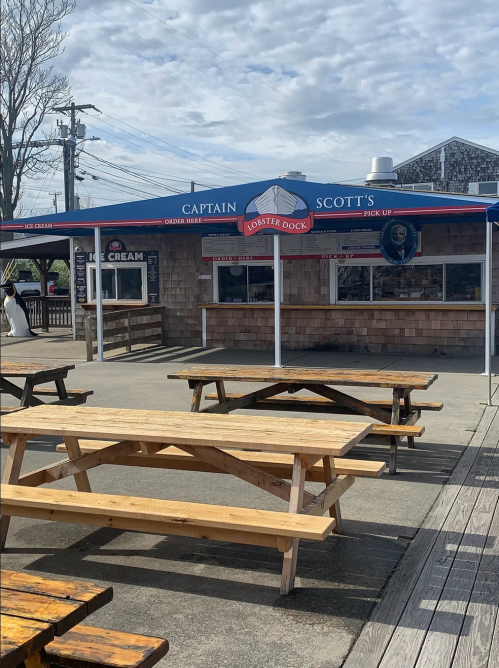 Outdoor view of Captain Scott's Lobster Dock with picnic tables and a blue awning, featuring an ice cream sign.