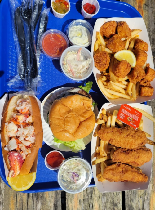 A blue tray with a lobster roll, burger, fried chicken, fries, coleslaw, and various dipping sauces.