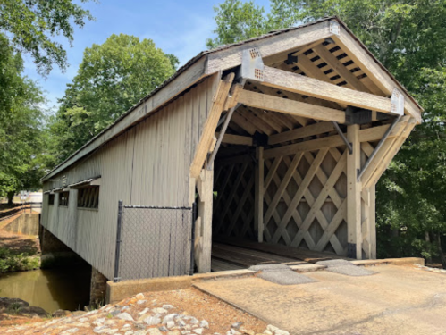 A wooden covered bridge with a lattice design, surrounded by trees and a small creek.