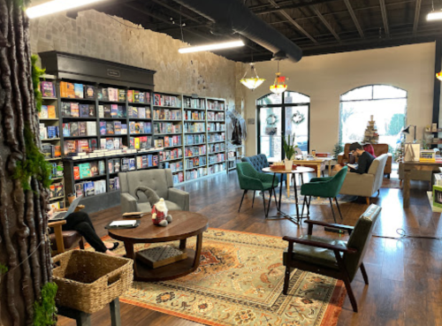 Cozy bookstore interior with bookshelves, seating areas, and a warm atmosphere, featuring a rug and decorative plants.