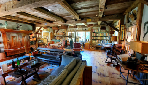 Cozy, rustic library with wooden beams, bookshelves, comfortable seating, and warm lighting.