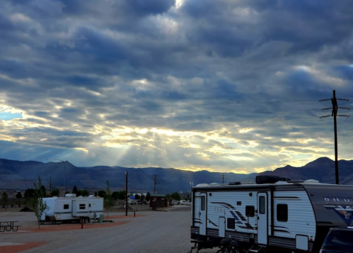 A scenic view of RVs parked under a dramatic sky with clouds and rays of sunlight breaking through. Mountains in the background.