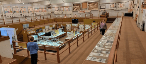 A spacious museum interior with exhibits and displays, featuring two visitors walking along a balcony.
