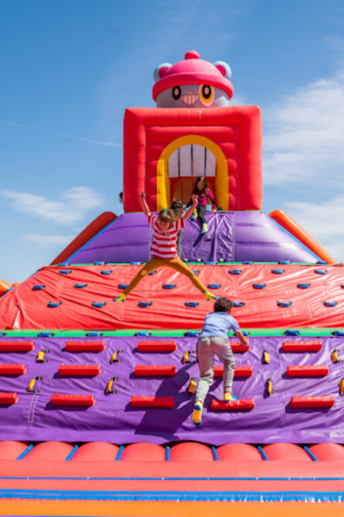 Children playing on a colorful inflatable slide and climbing wall under a clear blue sky.