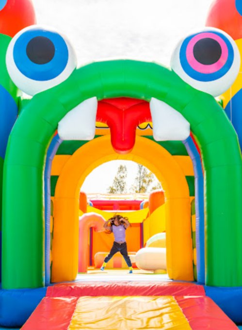 A child plays joyfully in a colorful inflatable bounce house with a whimsical monster design.
