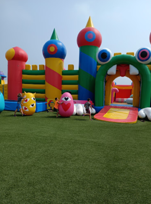 Colorful inflatable castle with playful designs, children running and playing on a grassy area.