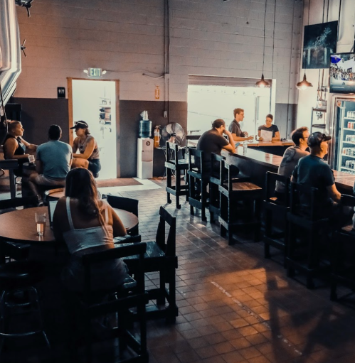 A casual bar scene with patrons seated at tables and the bar, enjoying drinks in a relaxed atmosphere.