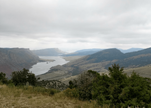 A scenic view of a winding river surrounded by mountains and rolling hills under a cloudy sky.