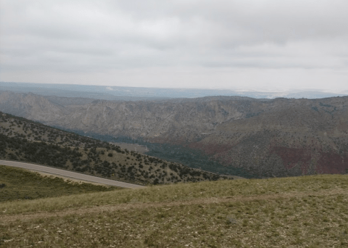A panoramic view of rugged mountains and valleys under a cloudy sky, with a winding road in the foreground.