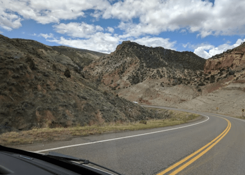 Curving road through rocky hills under a partly cloudy sky, showcasing a scenic mountainous landscape.