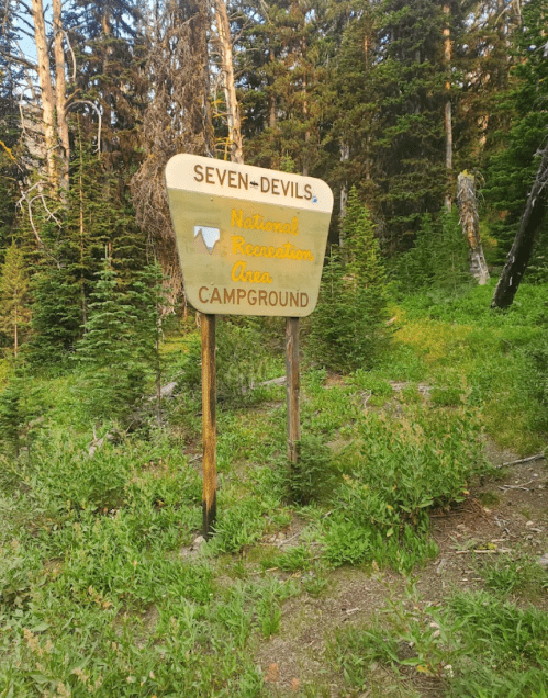 Sign for Seven Devils National Recreation Area Campground, surrounded by trees and greenery.