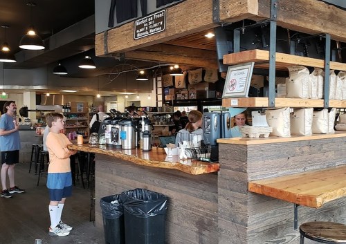 A cozy café interior with a wooden counter, coffee equipment, and customers ordering drinks.