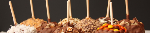 A variety of chocolate-covered caramel apples on sticks, topped with nuts, candy, and coconut.