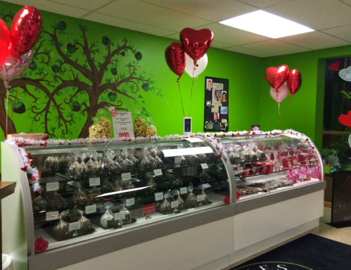 A colorful candy shop display with various chocolates and treats, decorated with heart-shaped balloons.
