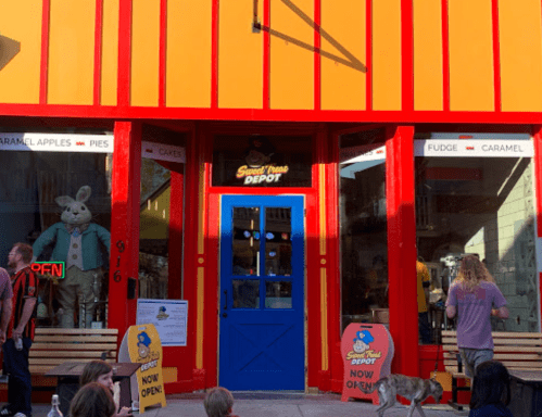 Brightly colored storefront with a blue door, featuring a bunny display, people outside, and signs for sweets.