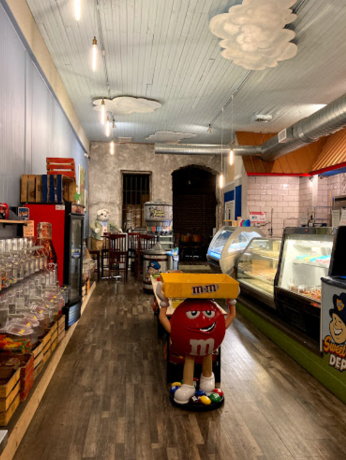 Interior of a colorful candy shop with a playful M&M character and various candy displays.