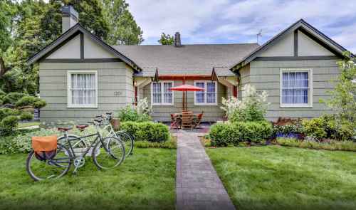 A charming green house with a red umbrella, surrounded by greenery and two bicycles parked in front.
