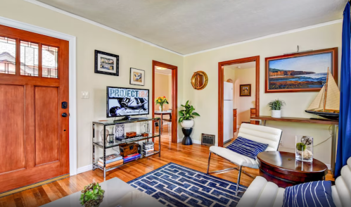 Cozy living room with a wooden door, TV, artwork, and nautical decor, featuring a blue and white rug.
