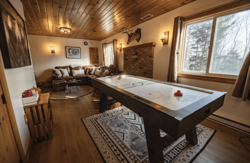 A cozy room featuring a wooden air hockey table, a comfortable seating area, and large windows with natural light.