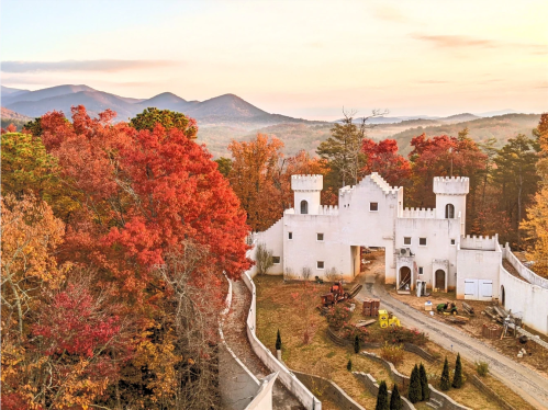 A white castle-like structure surrounded by vibrant autumn foliage and mountains in the background at sunset.