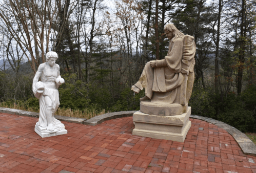 Two statues on a brick platform: one is a muscular figure, the other a seated, robed figure, with trees in the background.