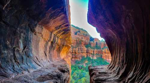 A stunning view of a canyon with colorful rock formations and greenery in the background, framed by two rocky walls.