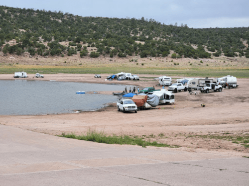A lakeside campsite with several RVs and tents, surrounded by greenery and a sandy shore.