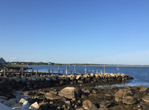 A serene coastal scene with a rocky shore, a dock, and calm waters under a clear blue sky.