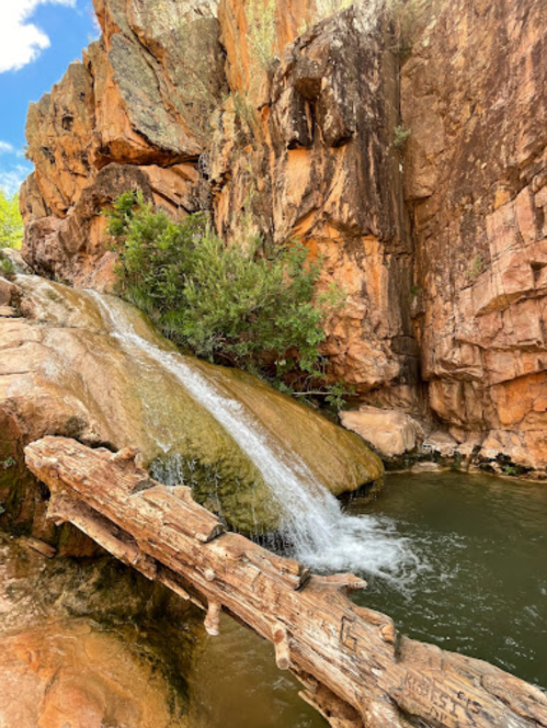 A serene waterfall cascades over rocks into a tranquil pool, surrounded by rugged cliffs and greenery.