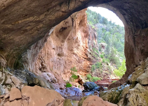 A natural rock arch frames a scenic view of a canyon with greenery and a stream below.